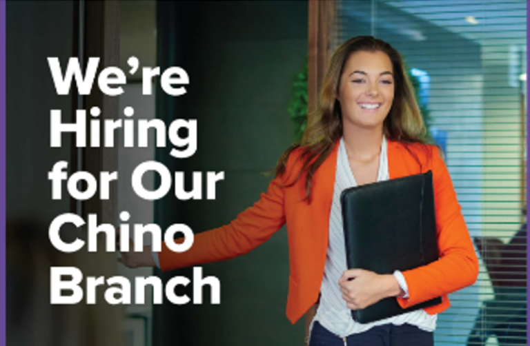 Smiling professional woman walking into office holding a folder with text overlay "We're hiring for our Chino branch"